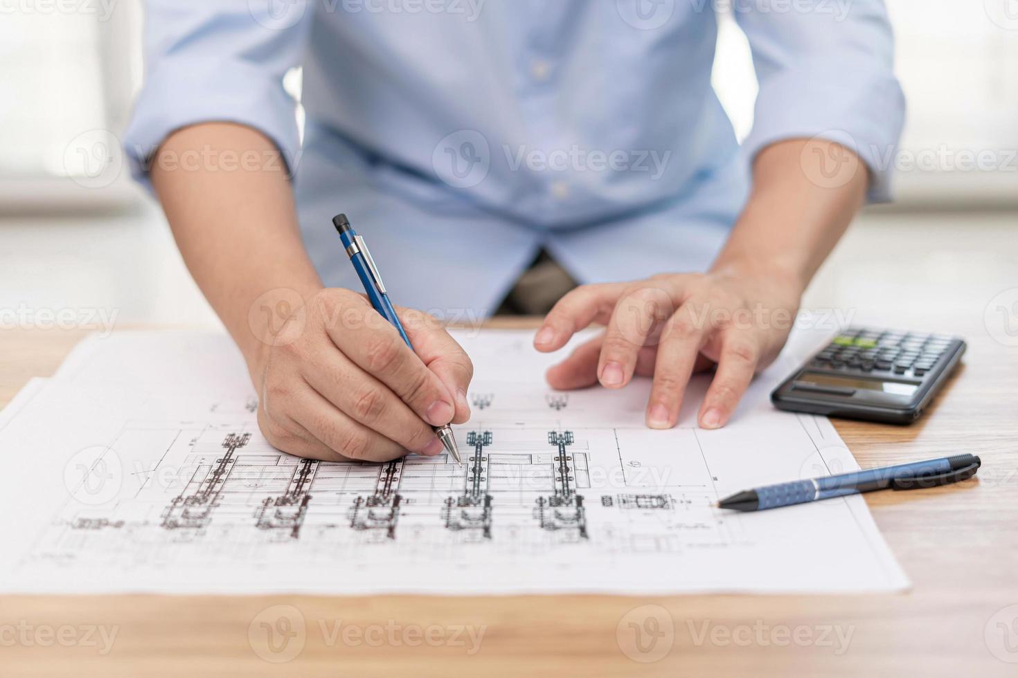 Engineering work concept  Close up hand a use pencil mark CAD drawing and calculator in Calculating document on the wood table photo