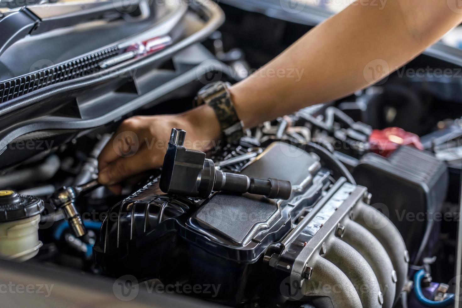 cierre la bobina de la bujía en la cubierta del motor y un hombre use una llave de bloque retire un perno para el servicio del motor de la bobina de despegue en el garaje y el fondo de la sala del motor foto