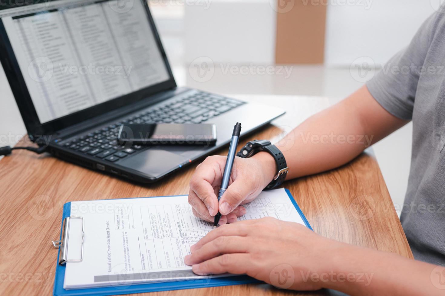 Service staff write on document about car repairs and use laptop online check part list on table in office photo