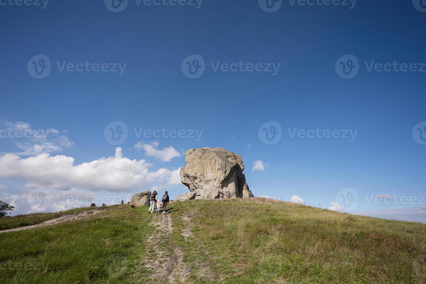 Kids exploring nature. Children wear backpack hiking with mother near big stone in hill. Pidkamin, Ukraine. photo