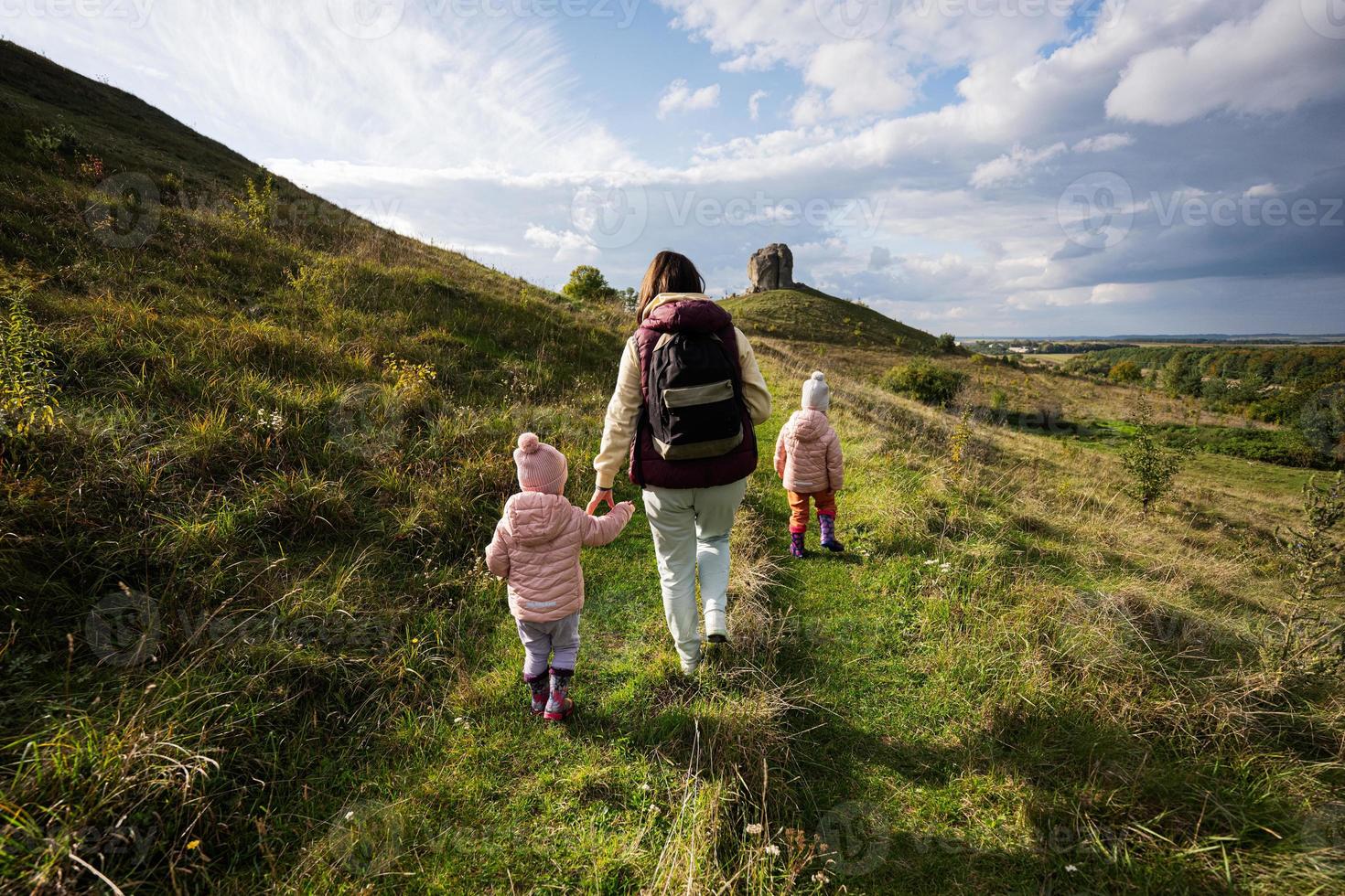 niños explorando la naturaleza. madre con dos hijas cerca de una gran piedra en la colina. pidkamin, ucrania. foto