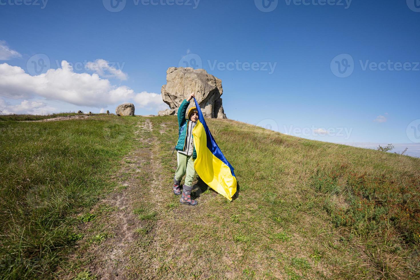 Welcome to Ukraine. Boy hold ukrainian flag near big stone in hill Pidkamin. photo