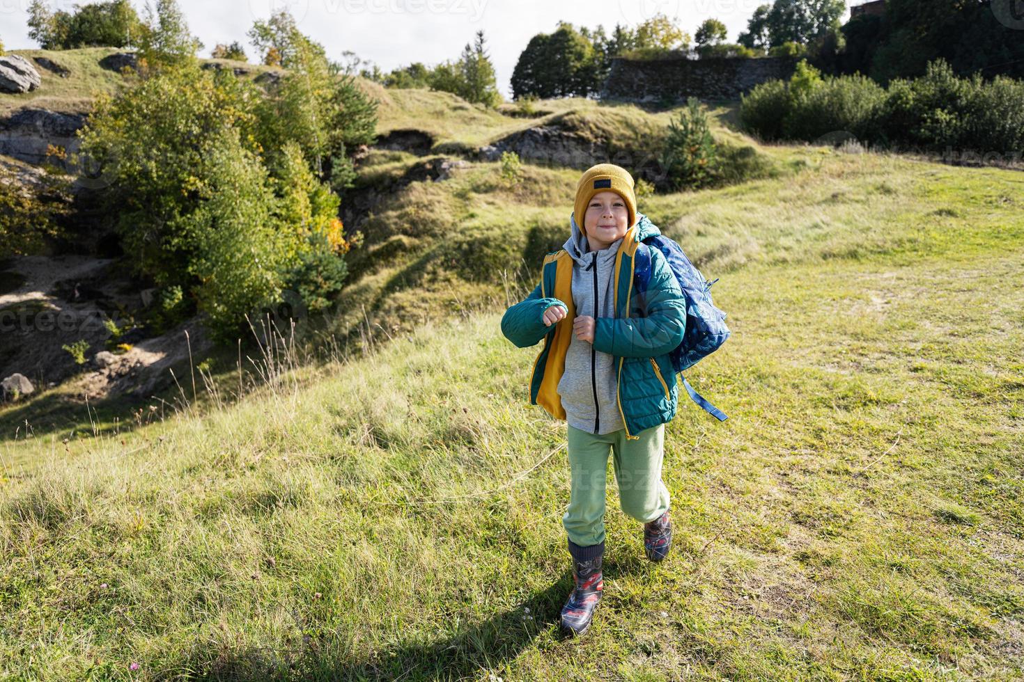 Activity on sunny autumn day, boy exploring nature. Kid wear yellow hat and backpack hiking. photo