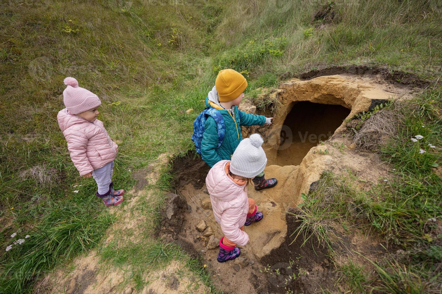 Three kids explore limestone stone cave at mountain. photo