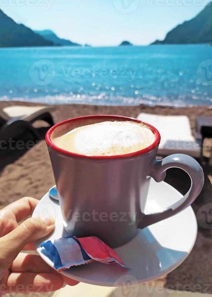 cup of coffee on the beach near the sea in sunny day photo