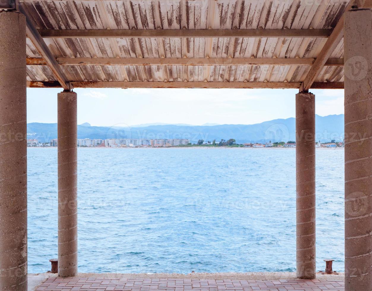 vista sobre un mar azul desde debajo de un toldo en un pequeño muelle de hormigón foto