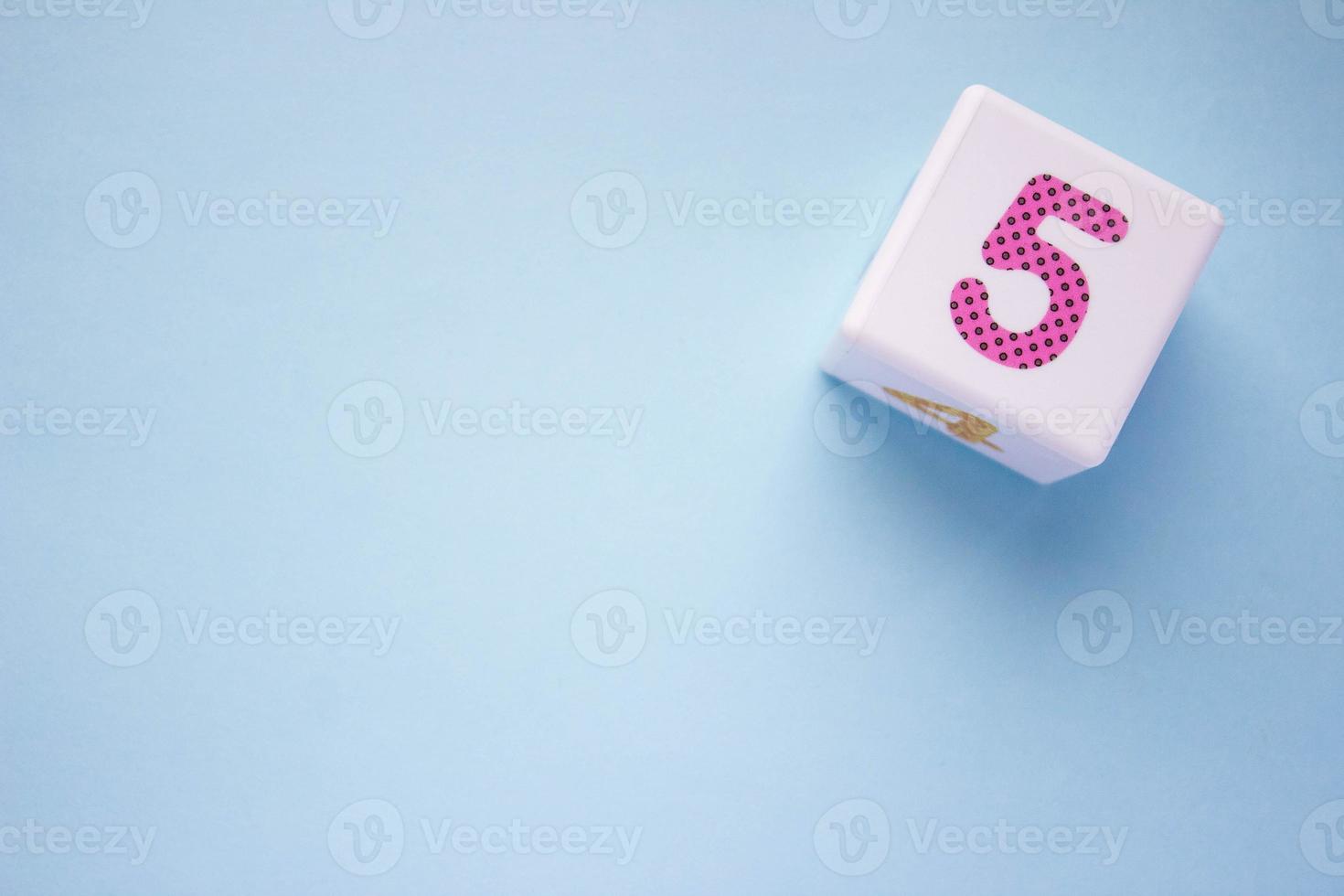 Close-up photo of a white plastic cube with a violet number 5 on a blue background in the upper right corner. With copy space