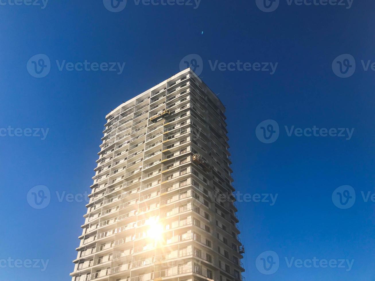 Large high reinforced concrete, panel, monolithic frame, frame-block house, building, skyscraper, new building with a glare of the sun in the windows against the blue sky photo