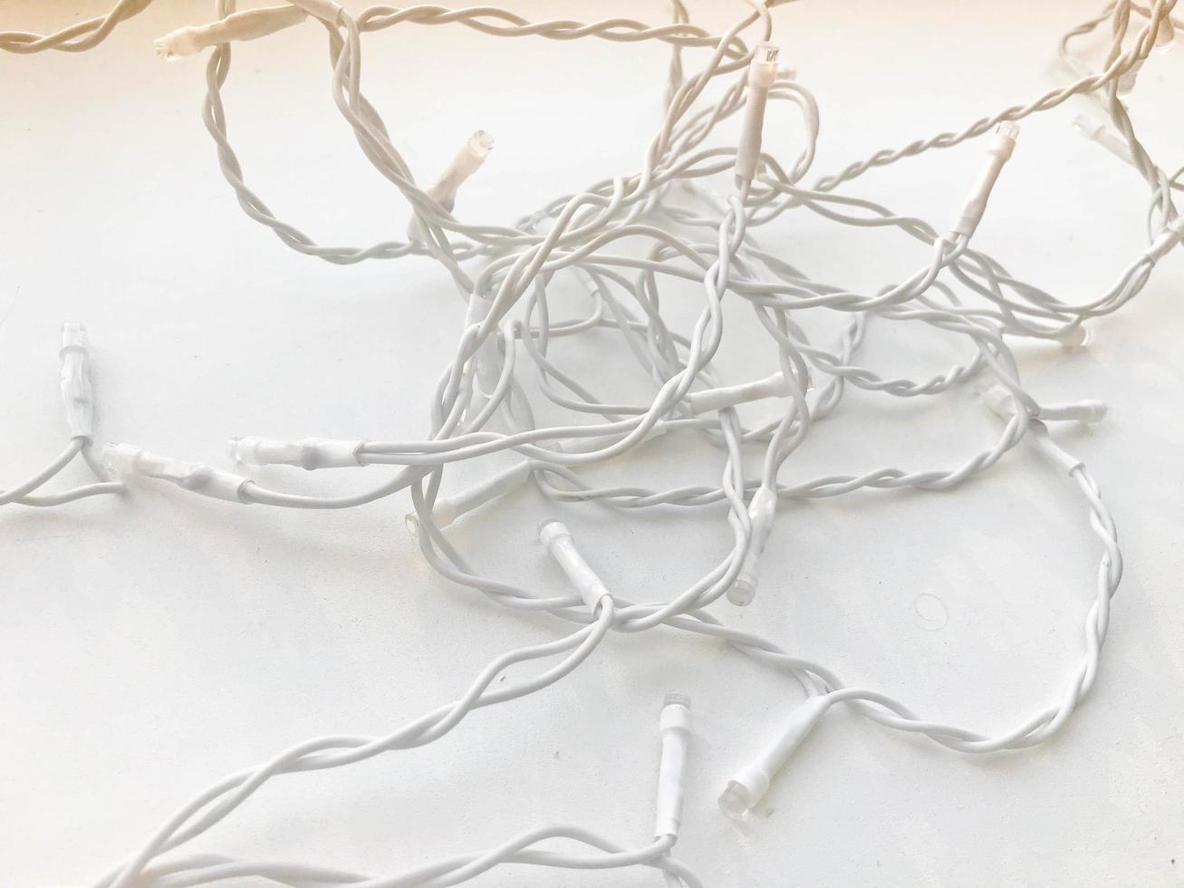 Twisted white wires of a garland in white rubber insulation with light bulbs on a white background photo