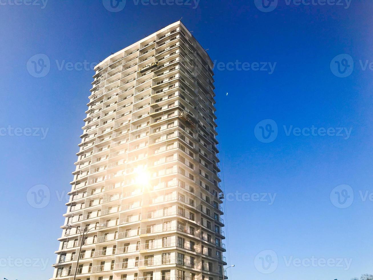 Large high reinforced concrete, panel, monolithic frame, frame-block house, building, skyscraper, new building with a glare of the sun in the windows against the blue sky photo