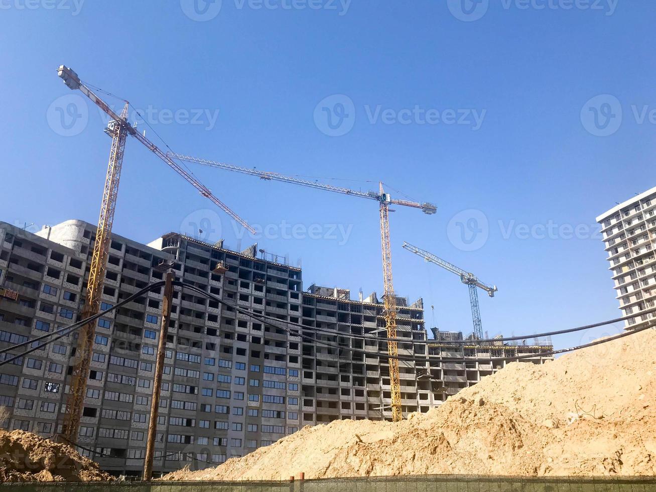 Building with the help of construction cranes of high reinforced concrete, panel, cast-frame, frame-block houses, buildings, skyscrapers, new buildings on the background of sandy land photo