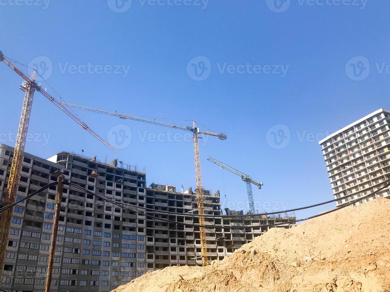 Building with the help of construction cranes of high reinforced concrete, panel, cast-frame, frame-block houses, buildings, skyscrapers, new buildings on the background of sandy land photo