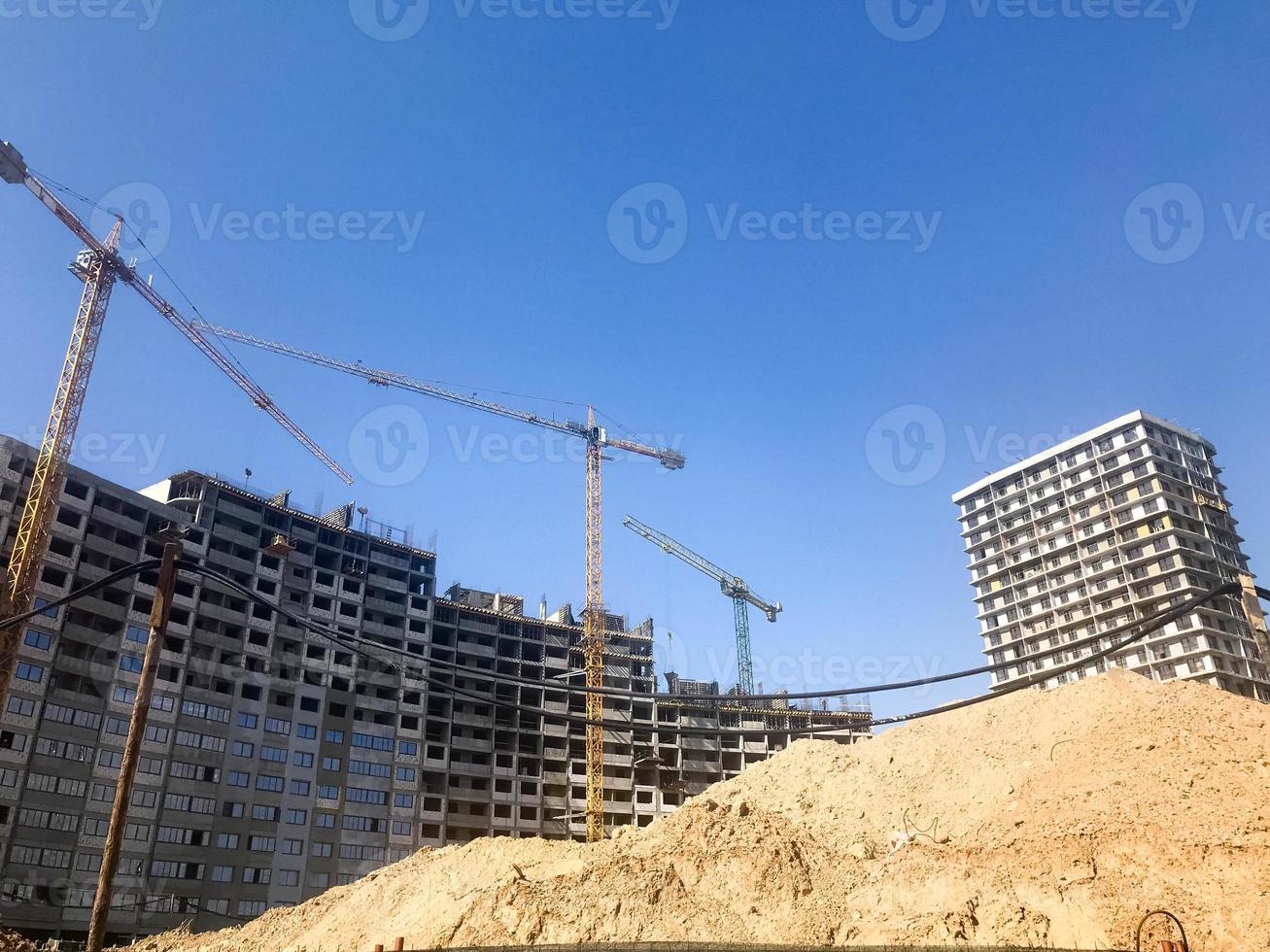 Building with the help of construction cranes of high reinforced concrete, panel, cast-frame, frame-block houses, buildings, skyscrapers, new buildings on the background of sandy land photo