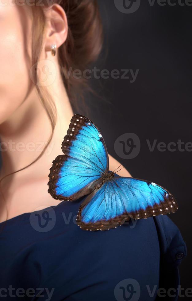 Close-up of a blue butterfly on a young girl's shoulder on a dark background. The concept fragility of nature photo