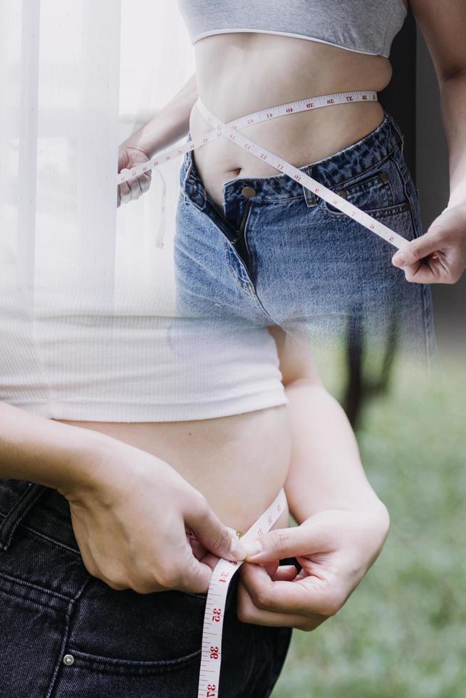 hermosa mujer gorda con cinta métrica usa su mano para exprimir el exceso de grasa que está aislado en un fondo blanco. ella quiere perder peso, el concepto de cirugía y descomponer grasa bajo el foto