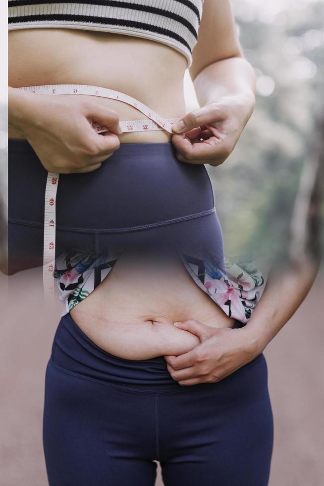 hermosa mujer gorda con cinta métrica usa su mano para exprimir el exceso de grasa que está aislado en un fondo blanco. ella quiere perder peso, el concepto de cirugía y descomponer grasa bajo el foto