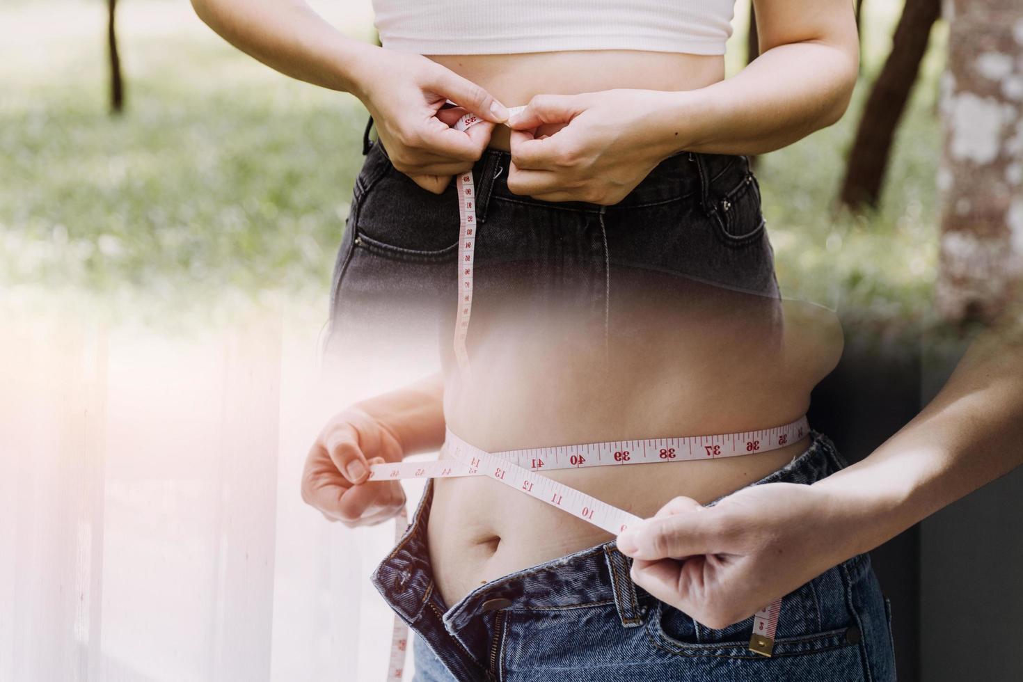 hermosa mujer gorda con cinta métrica usa su mano para exprimir el exceso de grasa que está aislado en un fondo blanco. ella quiere perder peso, el concepto de cirugía y descomponer grasa bajo el foto