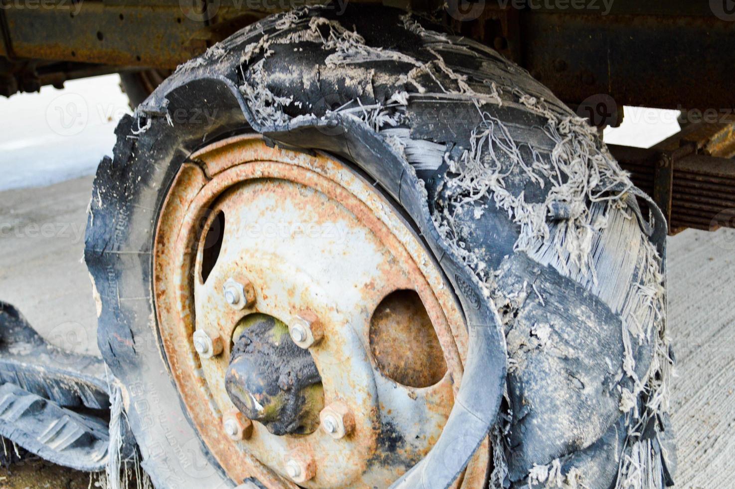 A large black rusty rubber wheel with a torn worn out broken bad old full of tires insecure tire photo