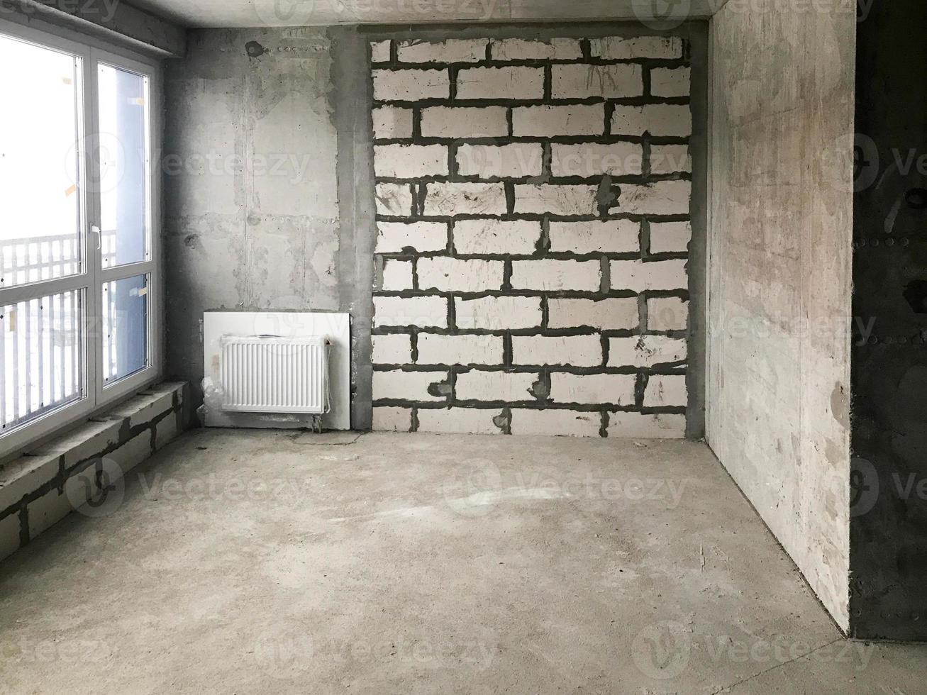 The apartment in the new building with a free layout without repair and decoration with bare walls and a large panoramic French window on the whole wall. Concept repair, housewarming, building photo