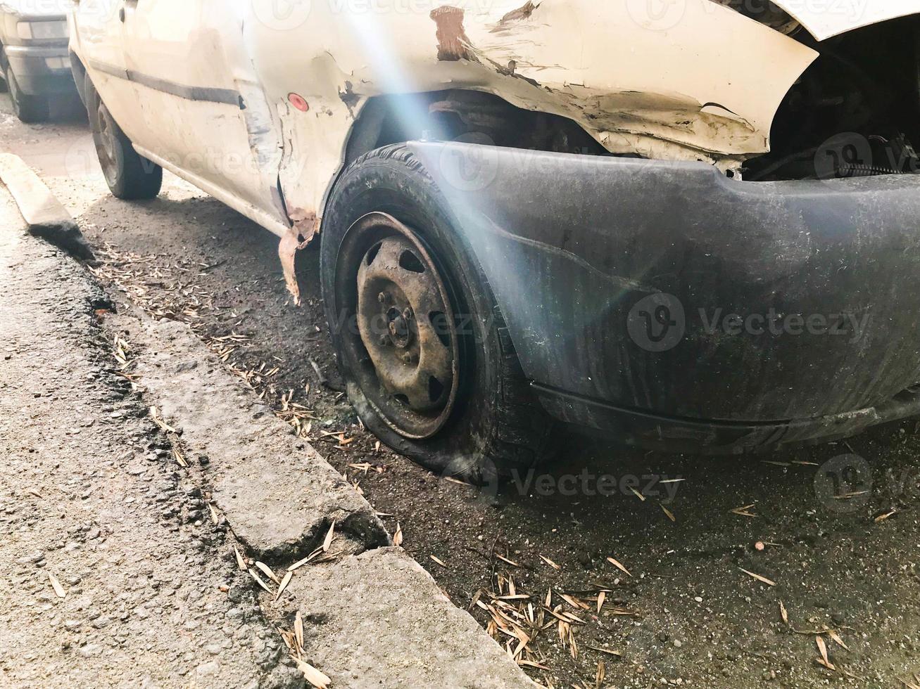 Old white rusty broken car of the carcass with lowered punctured wheels with scratches corrosion and a torn-off bumper with dents and scratches thrown on the road. Auto junk photo