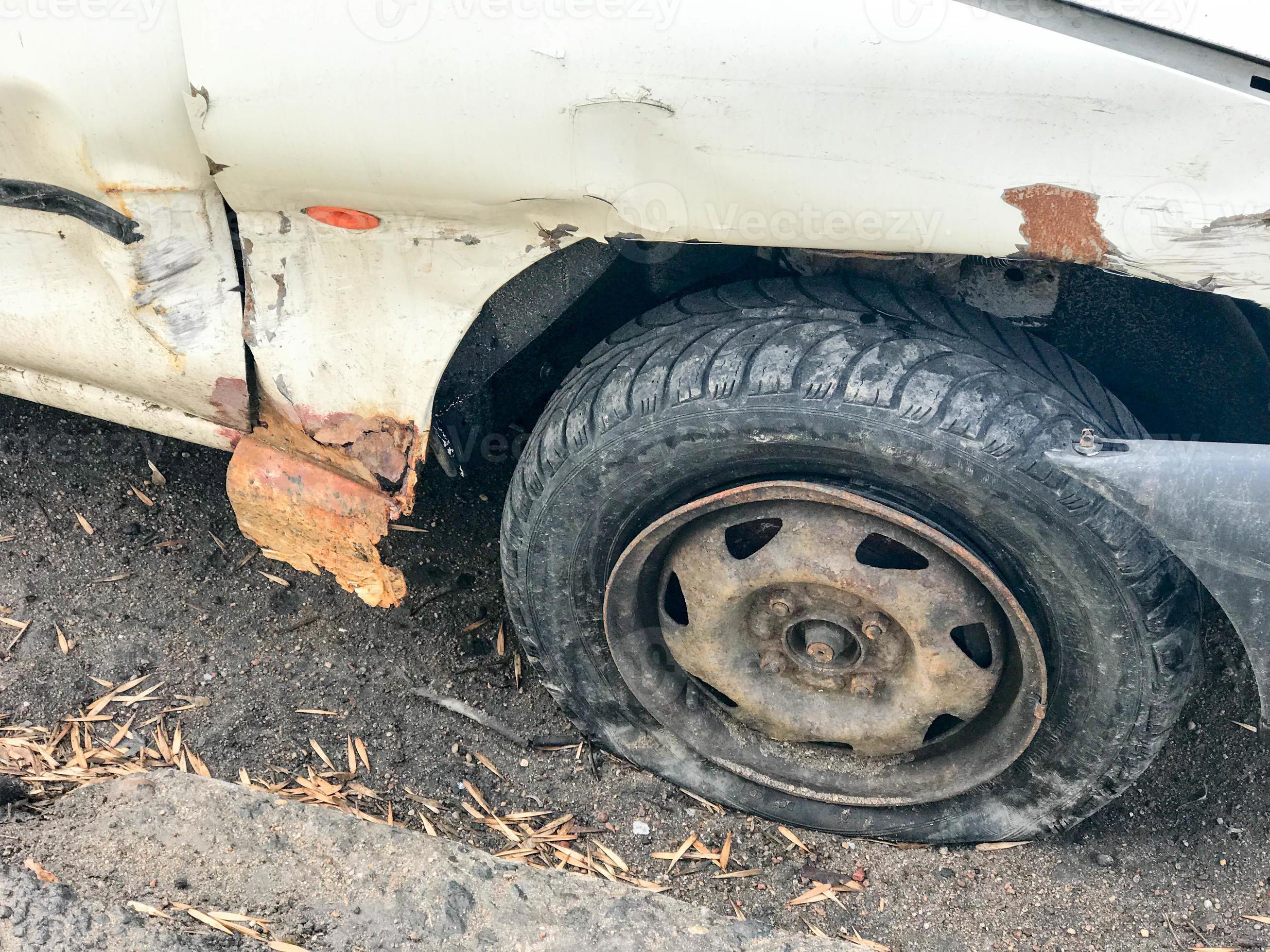 Old white rusty broken car of the carcass with lowered punctured wheels
