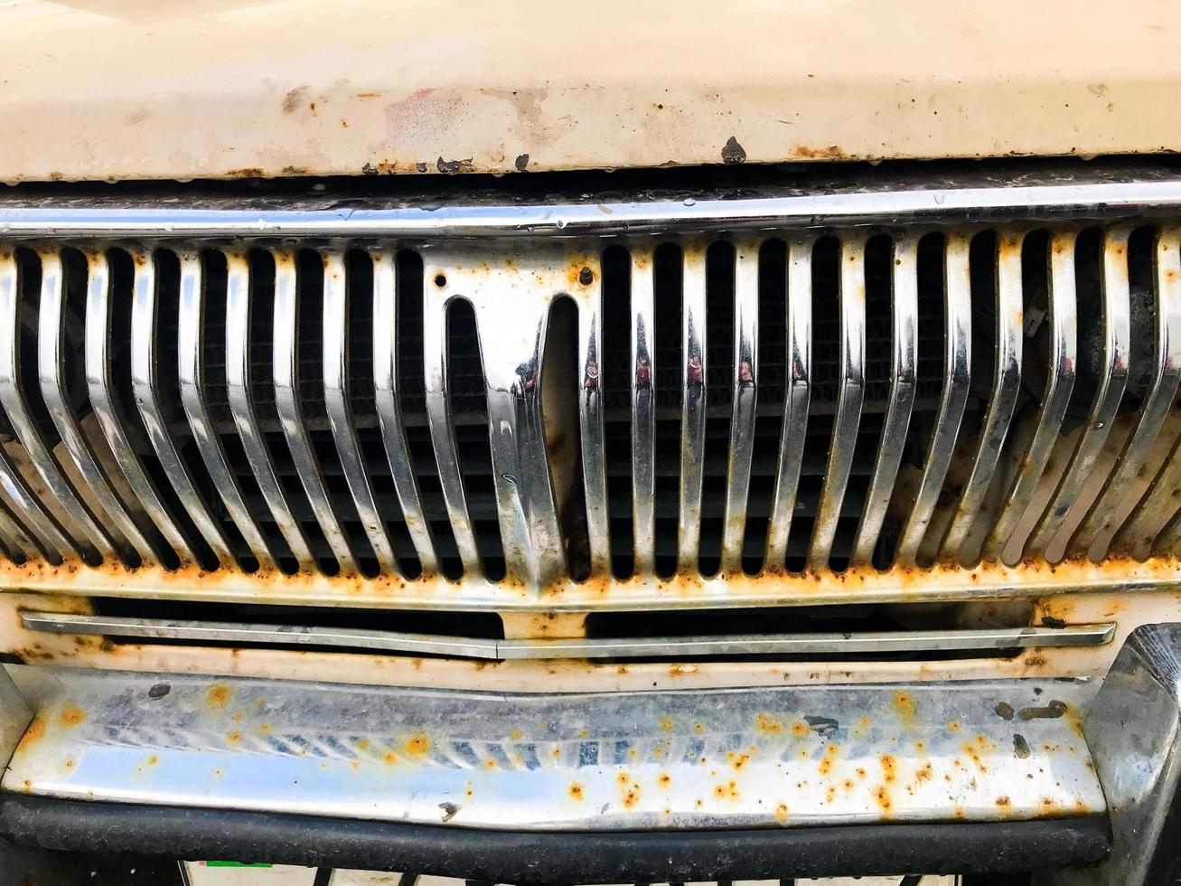 An old retro vintage hipster rusty oxidized chrome-plated metallic silver radiator grille in front of the retro hood of an antiquana white American passenger car from the 60s, 70s, 80s, 90s, 2000s photo