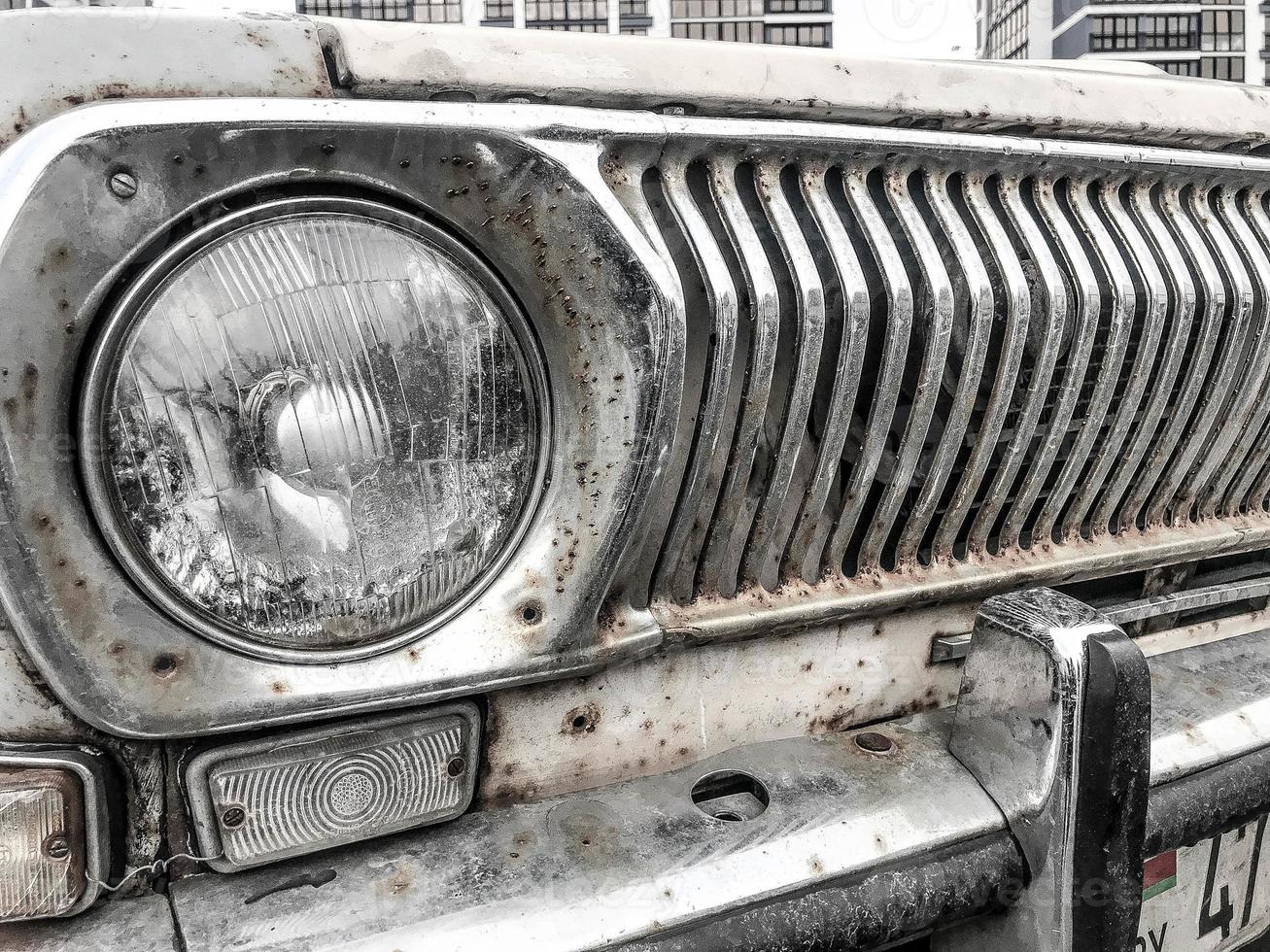 An old retro vintage hipster rusty oxidized chrome-plated metallic silver radiator grille and a round glass retro spotlight of an antiquan white white American car from the 60s, 70s, 80s, 90s, 2000s photo