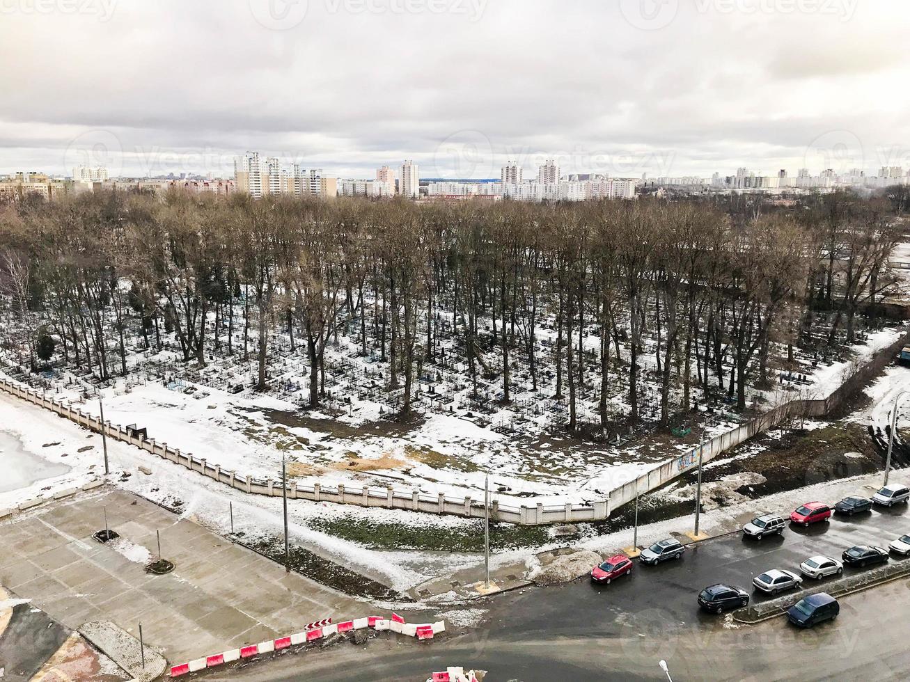 The view from the window of the old city cemetery in the park from a height with trees and houses in the winter. Panorama of the city photo