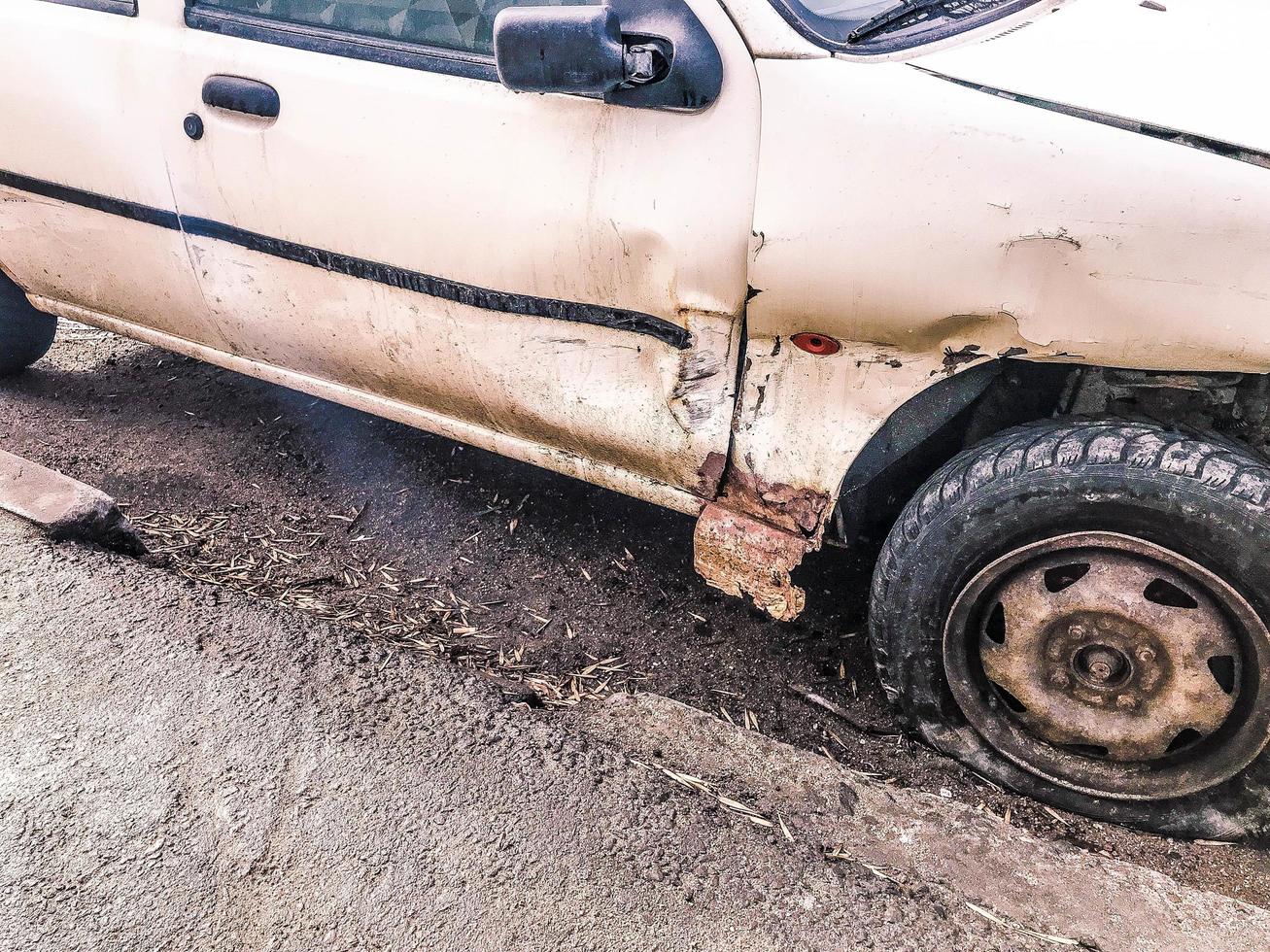 viejo coche blanco oxidado roto de la carcasa con ruedas pinchadas bajadas con arañazos corrosión y un parachoques roto con abolladuras y arañazos tirados en la carretera. chatarra de auto foto