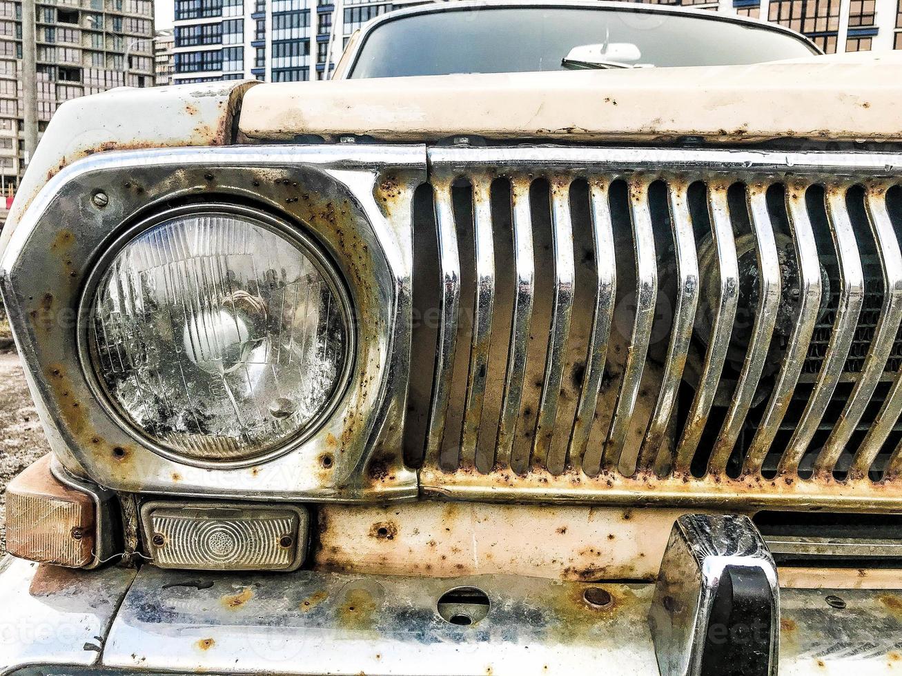 An old retro vintage hipster rusty oxidized chrome-plated metallic silver radiator grille and a round glass retro spotlight of an antiquan white white American car from the 60s, 70s, 80s, 90s, 2000s photo