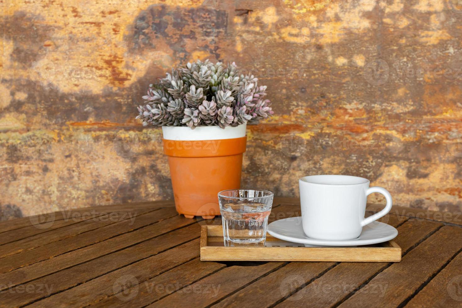 white coffee cup and glass of water on vintage wooden table and flower pot photo