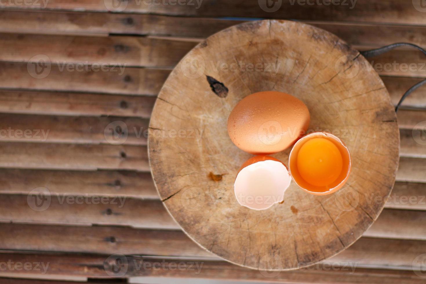huevos marrones en una tabla de cortar de madera hay una yema en la cáscara del huevo. el huevo marrón tiene una gota de agua porque se está sacando de la heladera. foto