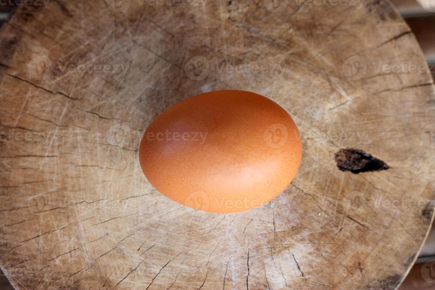 One raw brown egg laying on a wooden cutting board photo