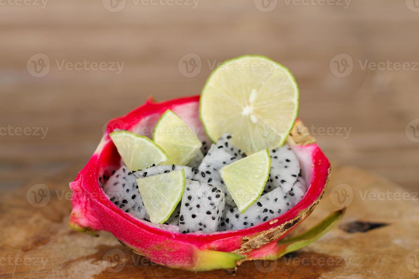 rodajas de fruta de dragón y rodajas de lima en un mango de cáscara de fruta de dragón sobre un fondo de mesa de madera antiguo. foto