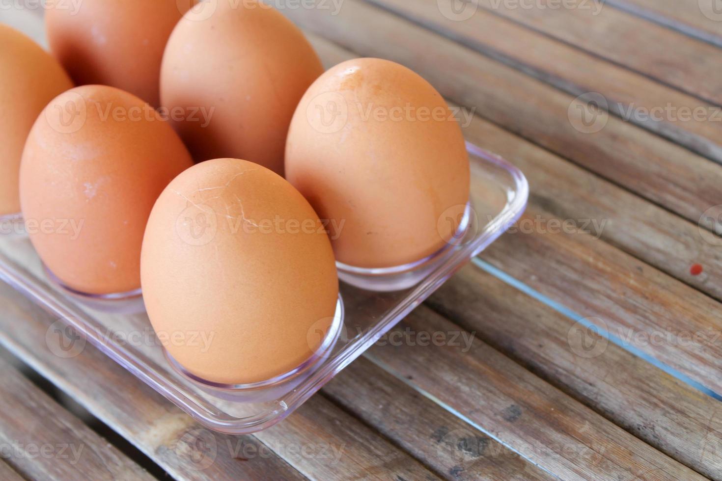close up Six brown eggs in plastic box on bamboo table with one broken boiled egg, top view. photo