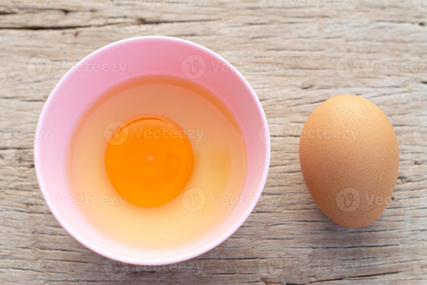 Broken egg shells and raw egg in small bowl  at wooden background for menu and recipe photo