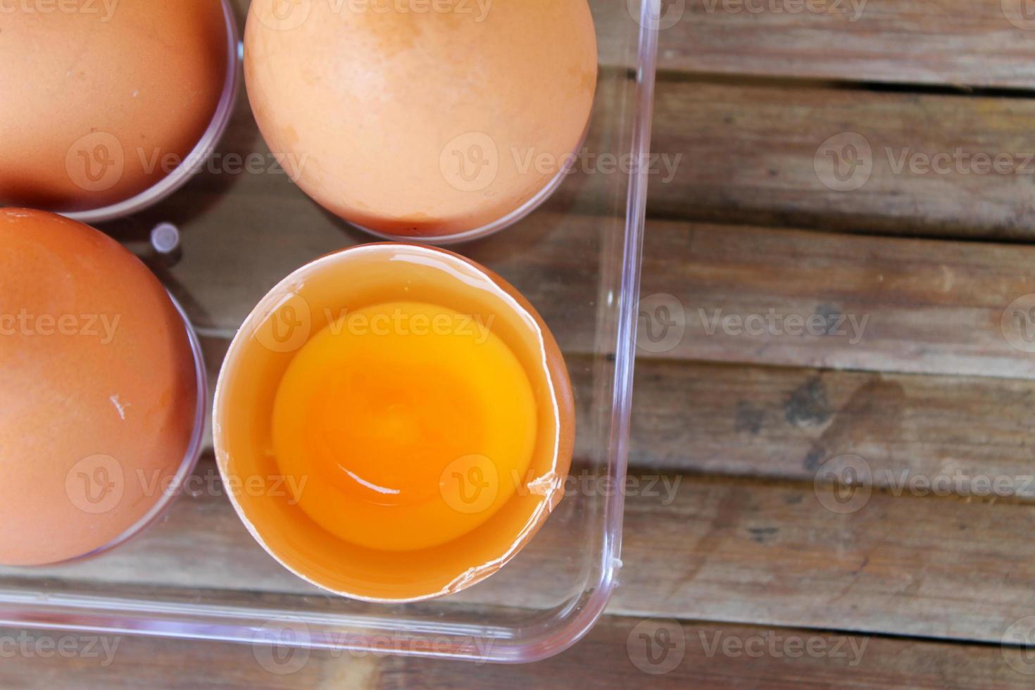 vista superior de la cáscara de huevo rota con yema amarilla cerca de los huevos en una caja de plástico foto