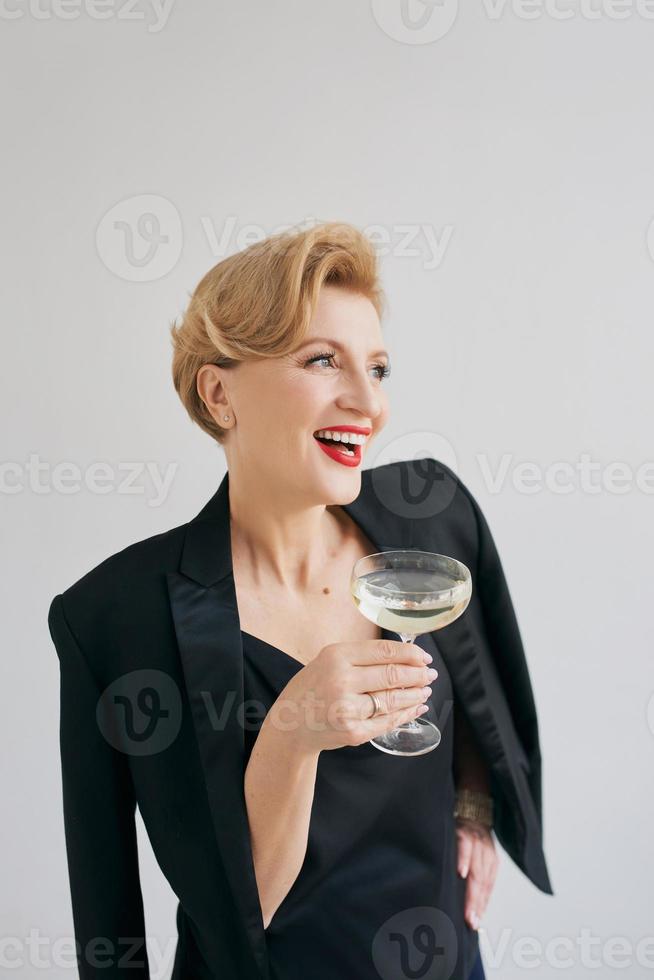 mujer madura elegante con estilo en esmoquin con una copa de vino espumoso. fiesta, celebración, concepto anti edad. foto