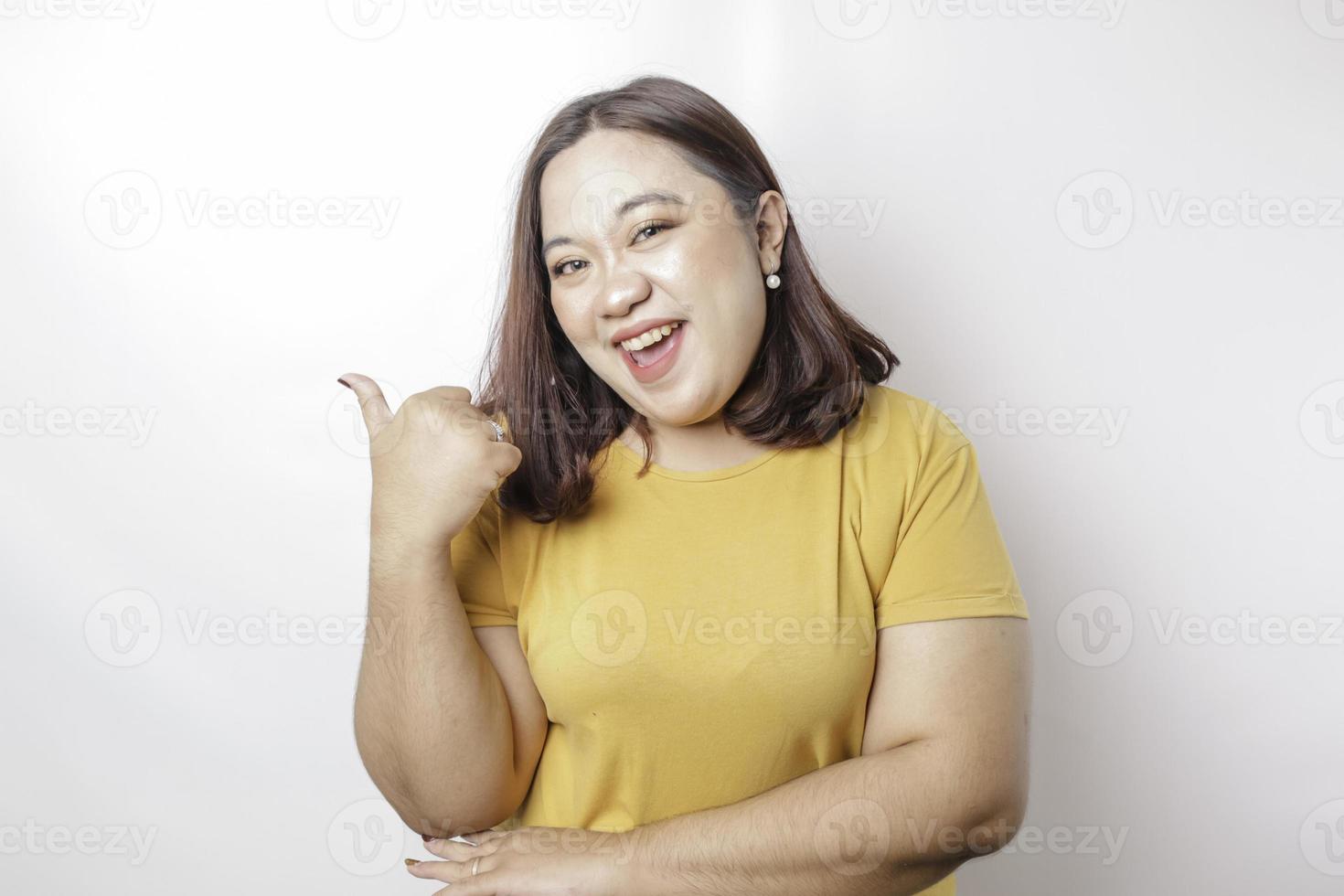 Excited Asian big sized woman wearing yellow shirt gives thumbs up hand gesture of approval, isolated by white background photo