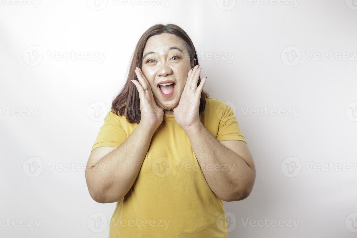 joven y hermosa mujer asiática de gran tamaño con una camisa amarilla gritando y gritando fuerte con una mano en la boca. concepto de comunicación foto