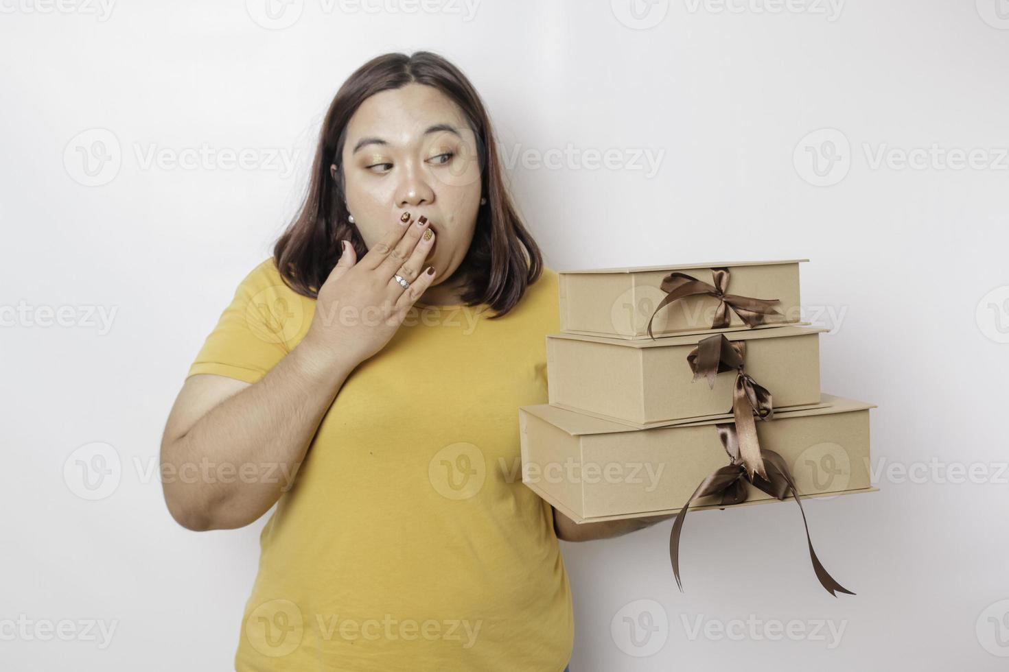 A shocked young Asian big sized woman is wearing yellow shirt and holding presents boxes and shopping bags. photo