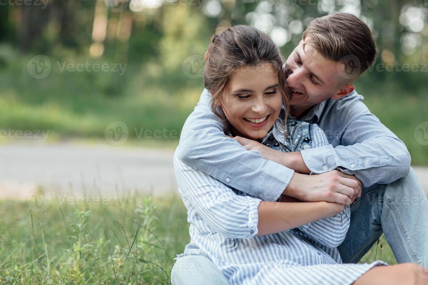 Outdoor shot of young happy couple in love sitting on grass on nature. Man and woman hugging, sunlight in summer park. Happy family in the evening sun light. The concept holiday photo