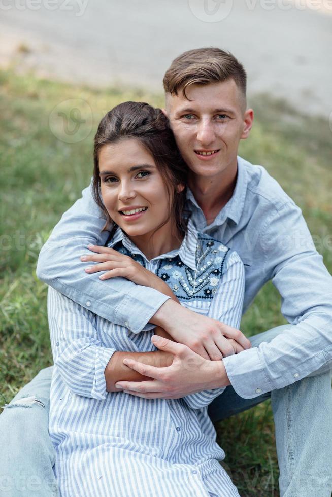 Outdoor shot of young happy couple in love sitting on grass on nature. Man and woman hugging, sunlight in summer park. Happy family in the evening sun light. The concept holiday photo