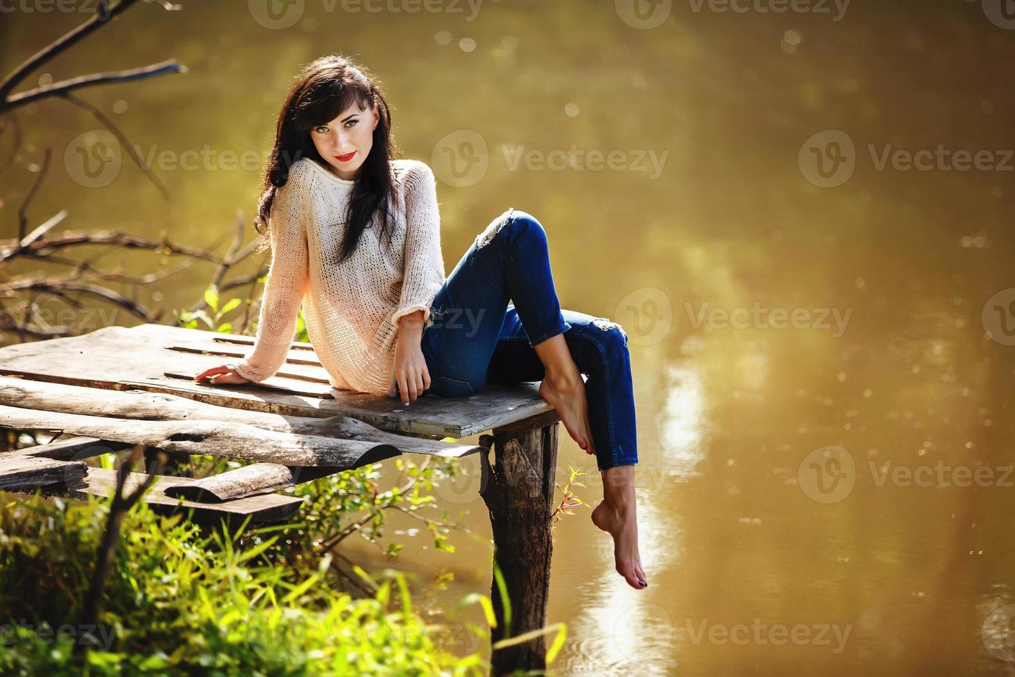Young woman sitting on the old bridge barefoot. Summer, green forest, lake and air in the evening bring the mood to relax, meditate, enjoy the sounds of nature and dream. photo