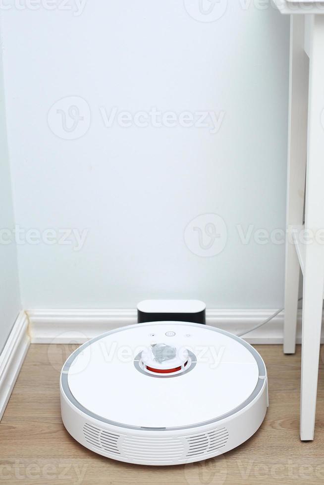 Robotic vacuum cleaner on laminate wood floor charging from base station. Smart cleaning technology. robot vacuum cleaner return to charging at dock in clean room floor photo