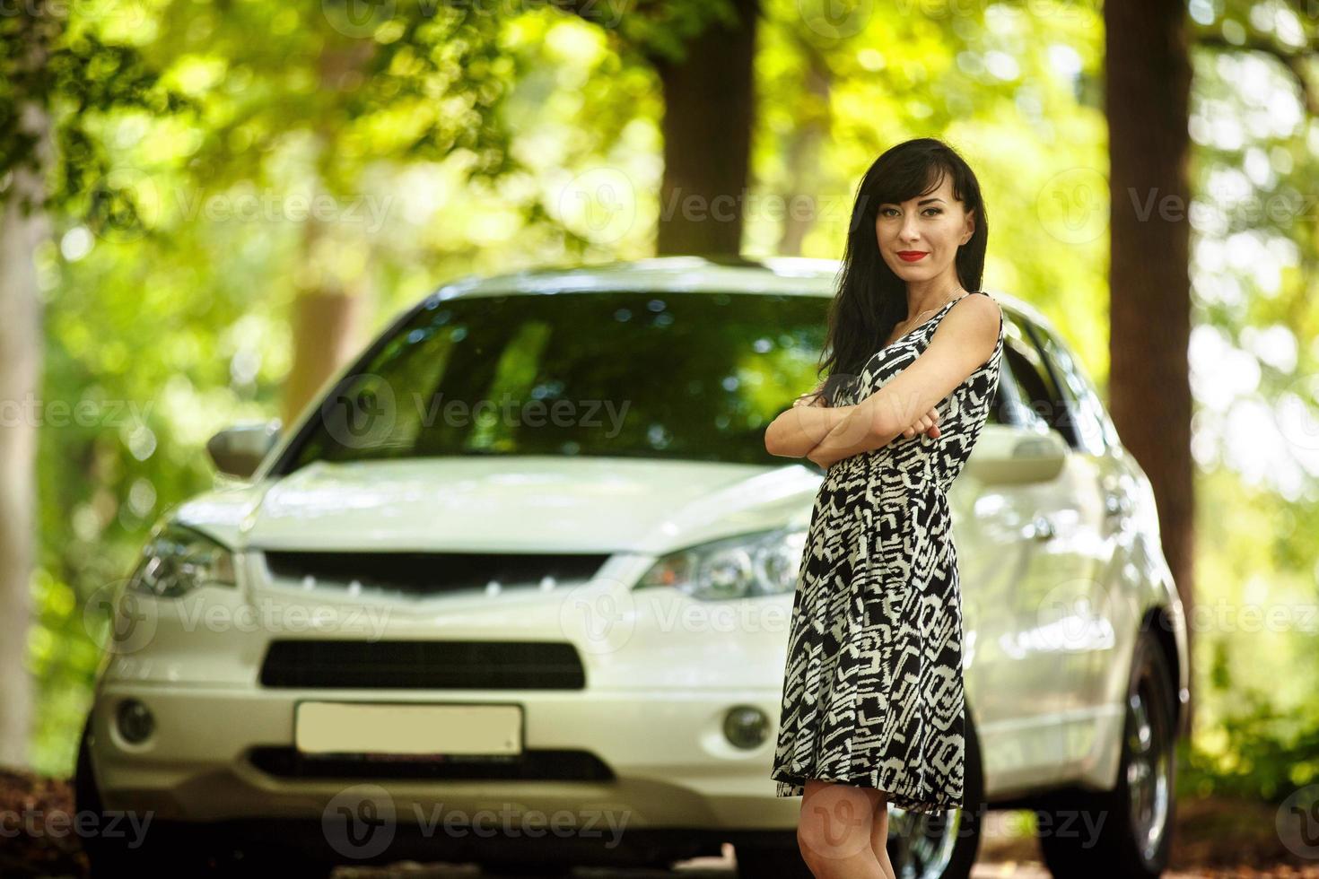 beautiful brunette in a dress posing in nature near a white car photo