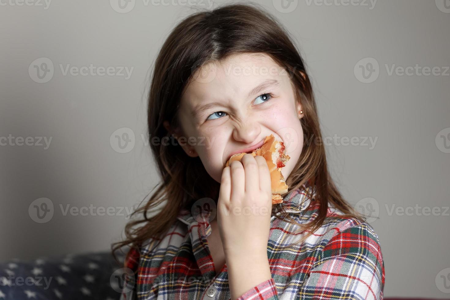 una linda niña comiendo emocionalmente una hamburguesa, un sándwich, una hamburguesa con queso o una hamburguesa y sonriendo en casa foto