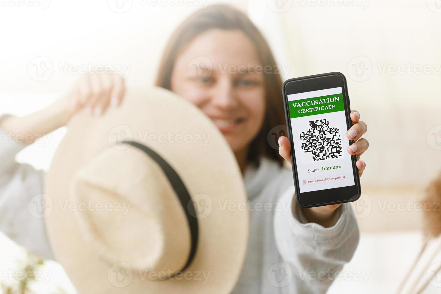 A defocused young girl is holding a passport and a smart phone with a certificate of vaccination against the Covid-19 disease. focus on the smart phone. Health Passport concept photo