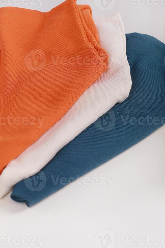 Pile of knitted warm colorfull sweaters with different knitting patterns folded in stack on white background, white wall background. Fall winter season knitwear. Close up, copy space for text photo