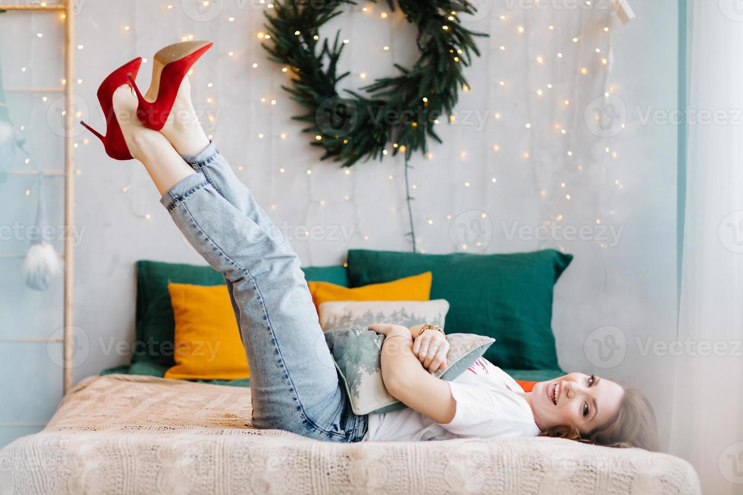 Portrait of gorgeous brunette woman in red high heels is having fun in bed and posing in the Christmas decorated interior. photo